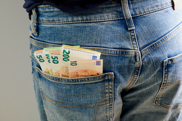 Cash tucked into the back pocket of denim jeans in a casual setting during daylight hours