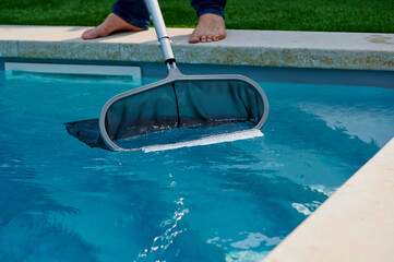 Cleaning leaves from a backyard swimming pool with a skimmer under bright sunlight