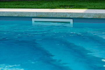 Swimming pool with clear blue water and pool cleaner in well-maintained backyard setting during sunny day