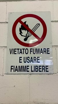 Close-up shot of a sign displaying 'Vietato Fumare e Usare Fiamme Libere' an Italian phrase for 'No Smoking and No Open Flames,' against a neutral backdrop.