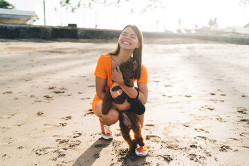 Brunette woman in orange activewear performs stretching exercises on beach, representing fusion of...