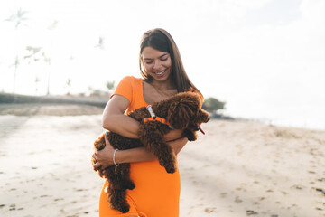 Brunette woman in orange sports attire practices tai chi on beach, exemplifying integration of...