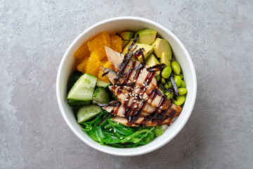 A beautiful arrangement of a nutritious bowl filled with fresh greens, grilled chicken, avocado, edamame, and orange slices