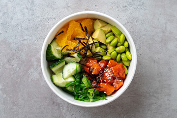 A beautifully arranged bowl features salmon, avocado, cucumbers, oranges, and edamame, garnished with seaweed and sesame seeds, evoking a taste of the sea. Perfect for lunch or dinner