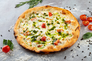 A delicious pizza rests on a textured surface, artfully topped with melted cheese, cherry tomatoes, fresh herbs, and vibrant green pesto. The inviting aroma beckons pizza lovers