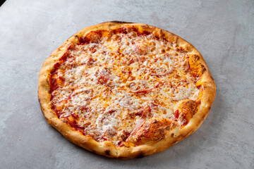 A delicious round pizza topped with melted cheese and savory toppings sits on a gray surface, inviting hungry guests to indulge in its warm, comforting flavors during a casual dining experience