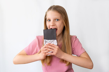 Naklejka premium Girl eating large chocolate bar happily. Excited young girl with long blonde hair and pink shirt about to bite into a big dark chocolate bar in foil wrapping.