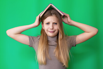 Frustrated student with book on head. Teen girl with a humorous frustrated expression balancing a book on her head against a bright green background, suggesting study stress.