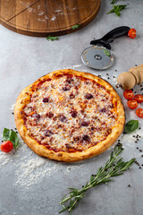 A mouthwatering pizza sits on a flour-dusted surface, showcasing golden crust and melted cheese, surrounded by fresh basil, herbs, and cherry tomatoes alongside a rolling pin