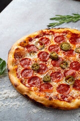 A mouthwatering pepperoni pizza topped with spicy jalapenos sits on a rustic gray surface. The vibrant colors of the toppings draw attention, promising a delightful culinary experience