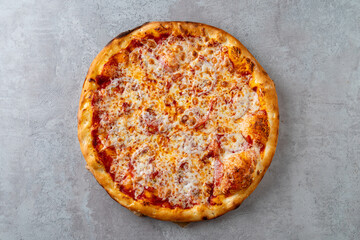 A warm, cheesy pizza sits on a gray surface, showcasing a perfectly baked crust and bubbling cheese. Ideal for sharing, it's an inviting meal for gatherings and celebrations