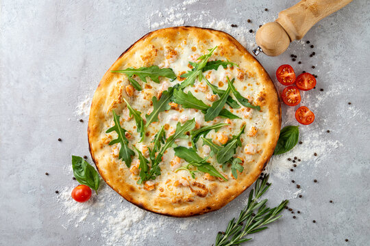 Warm, golden crust of a white pizza features vibrant arugula and ripe cherry tomatoes, all artistically arranged on a rustic surface sprinkled with flour and herbs