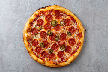 A mouthwatering round pizza features generous layers of pepperoni and spicy jalapenos on a perfectly baked crust, creating an inviting dish perfect for sharing with friends or family