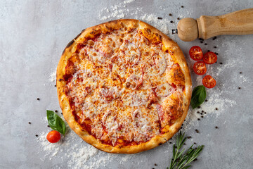 A freshly baked pizza lies on a rustic countertop, surrounded by cherry tomatoes, basil leaves, and...