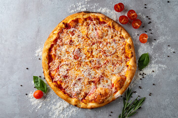 A deliciously baked pizza sits on a rustic gray surface, adorned with gooey cheese, cherry tomatoes, and vibrant basil leaves, evoking a homemade culinary delight