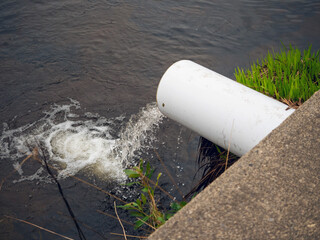 Clean water runs from white plastic pipe into river. Result of water plant work. Keeping nature...