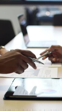 A medium close-up video of diverse hands with varying skin tones, pointing and tracing intricate data visualizations on crisp paper and a bright digital tablet on a modern office conference table,
