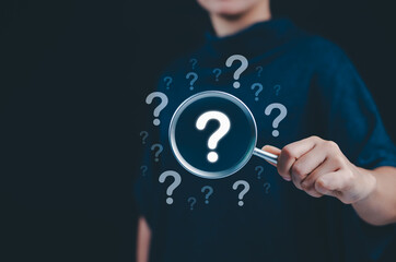 Question mark and root cause analysis concept. A hand holding a magnifying glass over large...