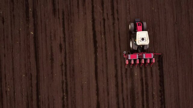 Red tractor pulls seeder creating precise parallel rows