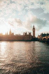 Fototapeta premium Iconic view of Big Ben with a red double-decker bus and the London Eye in the background on a cloudy day in London.