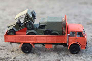 Side view of a scale model of an orange Soviet cabover truck that transports army SUVs.