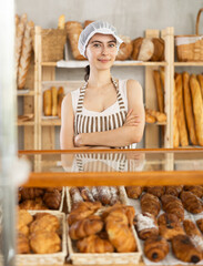 Young woman seller in apron at counter with pastries in bakery