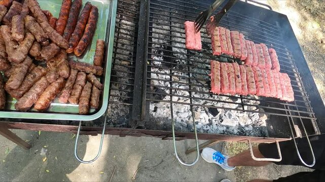 meat on the grill a barbecue grill where chevaps (a Balkan dish made from meat) are being fried on coals on a metal grate, a man's hand turning them over