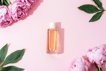 Perfume bottle and pink peony flowers on light pink background with shadows. Top view, flat lay