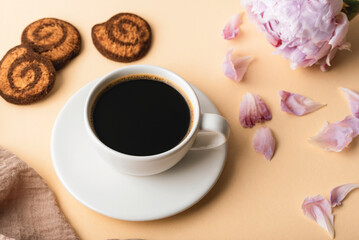 Coffee cup, handmade cookies and peony flower with petals on beige background, top view
