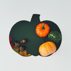 Creative flat lay of decorative pumpkins, acorns and autumn leaves visible through a pumpkin shaped gap. Cozy seasonal concept for fall backgrounds, Thanksgiving themes and harvest celebrations.