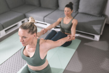 Obraz premium Women practice partner yoga in a modern indoor studio with comfortable seating and neutral tones