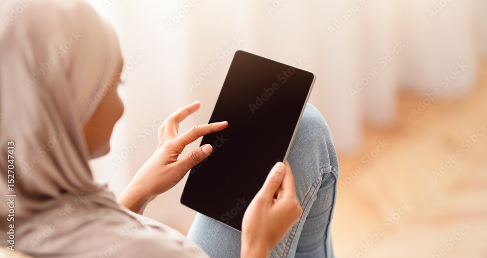 Poster black arab woman in hijab using tablet computer with empty screen while sitting in cozy armchair at 