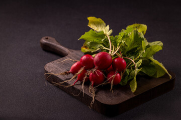 Fresh radishes with green leaves resting on dark cutting board