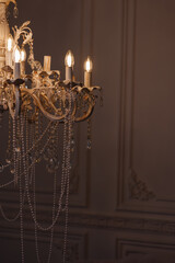 Close-up of ornate vintage chandelier with pearls and lit bulbs against dark classic wall, right...