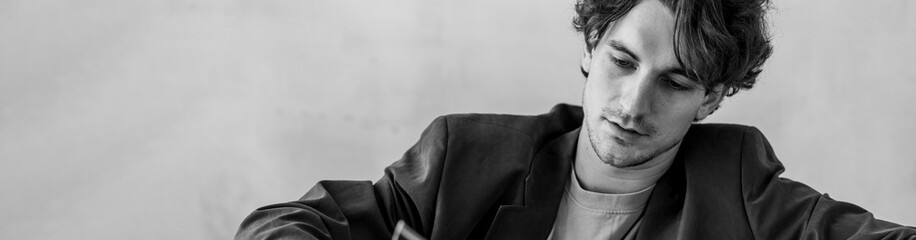 Banner. Black and white portrait of strong healthy elegant handsome sexy athletic man in leather coat in a stylish loft interior, wearing suit, watches. Male model posing and smiling