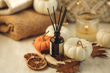 Cozy interior with knitting, burning candles and aroma perfume diffuser in the living room. Fall pumpkin pie fragrance, cinnamon, anise, dry citrus, leaves. Home comfort, coziness, aromatherapy