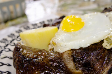 A serving of beef with fried egg and potatoes, most of the meal is out of focus