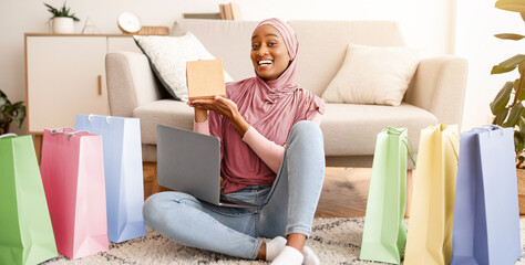 Online shopping and delivery concept. Pretty Muslim lady in hijab sitting on floor surrounded by...