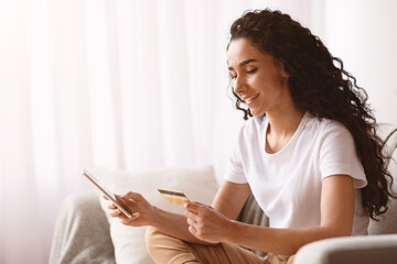 Side view of pretty young lady shopping online with modern smartphone and credit card, ordering...