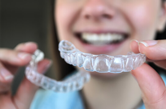 Mujer sonriendo y sujetando contenciones dentales 3d de ambos maxilares para tratamiento de ortodoncia.