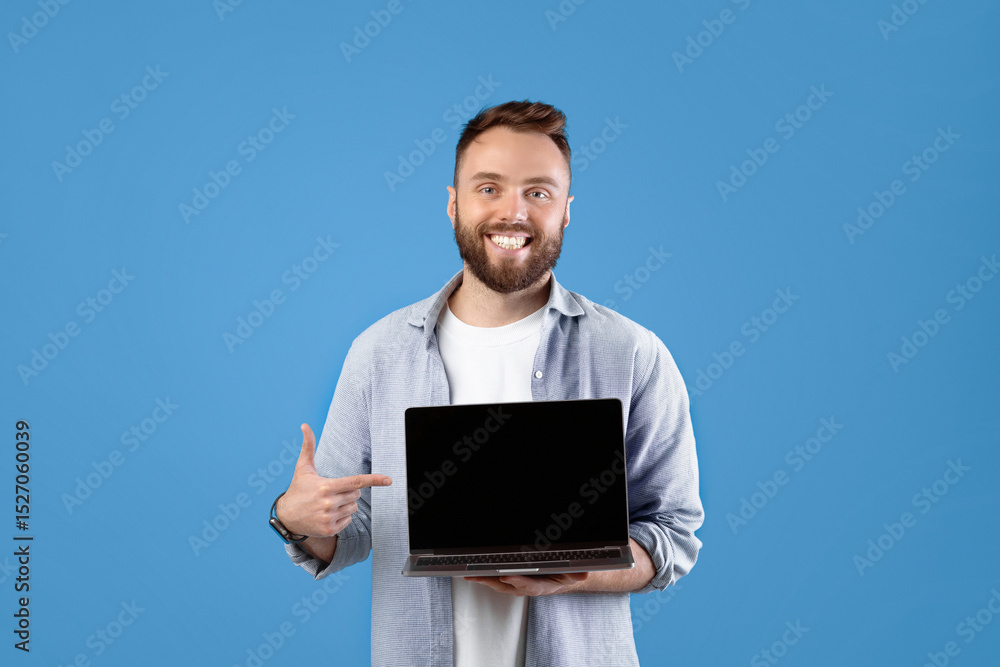 Poster portrait of happy bearded man holding laptop computer with empty screen over blue studio background,