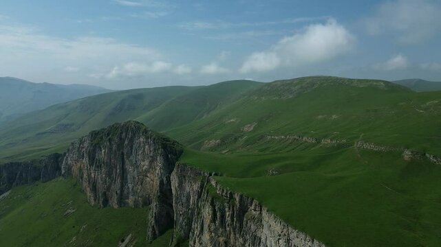 Beautiful panoramic view of green mountains with rocky formations, covered in lush grass, captured by drone against a clear blue sky.
