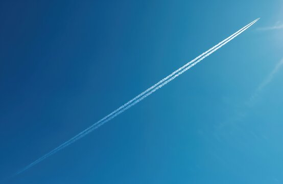 Bright blue sky with jet contrail. Aeroplane trail across clear sky. White vapor trail of an aircraft flying high. Travel air transport concept. Flight path over clouds. - Powered by Adobe