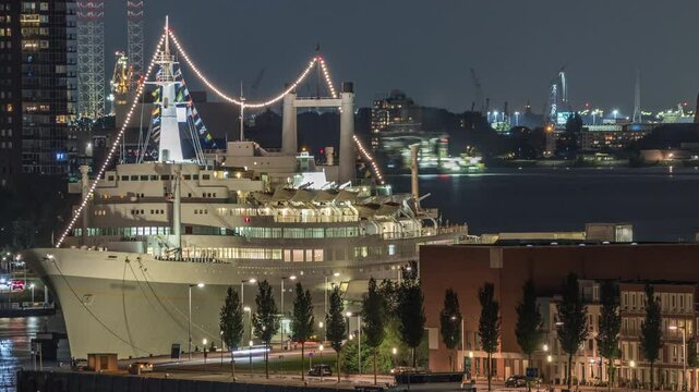 Aerial timelapse of Maashaven harbour at night in Rotterdam, The Netherlands. Features the illuminated waterfront skyline and the SS Rotterdam, a former cruise ship now a hotel, moored at Katendrecht