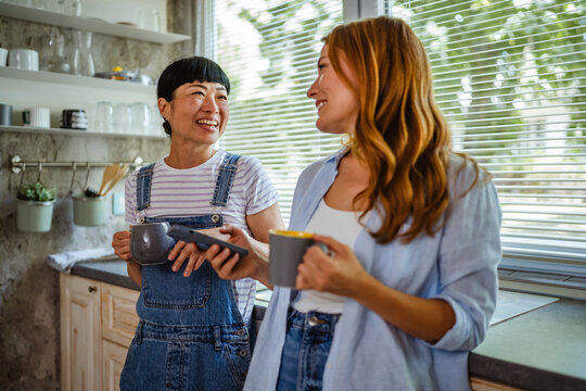 two diverse female friends use mobile phone and have fun at home