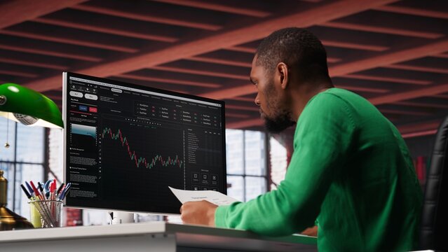 African american man using PC to purchase and sell stocks, monitoring forex graphs and diagrams. Male broker looking at stock exchange candle stick charts on computer. Camera A.