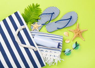 Blue beach bag with summer accessories on color background, top view