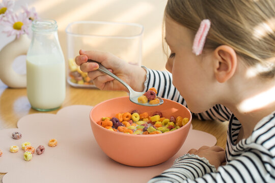 Cute little girl eating colorful circle cereal with milk for breakfast. Dry cereal for breakfast