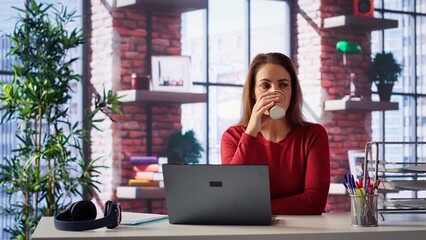 Casual focused woman sitting at her desk and reading research papers, multitasking with laptop at...