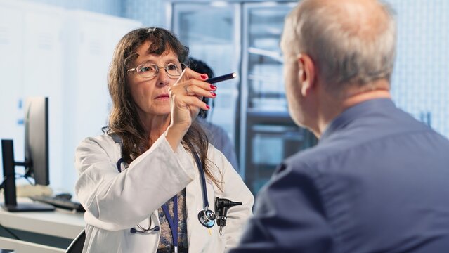 Professional medic examining patient reaction to light for pupil response during concussion assessment, checking for dizziness, light sensitivity and balance issues. Trauma checkup. Camera B.
